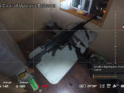 A screenshot from drone footage shows a rifle set up on a table in an upstairs bedroom.