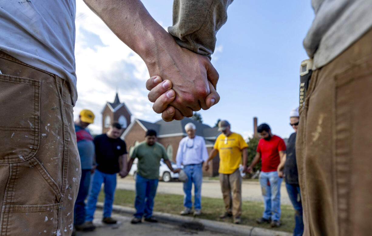 Members of IChurch from Hickory, N.C., pray Oct. 5 with Bob Smith, center, a Trustee of the Old Fort United Methodist Church in Old Fort, N.C. More than four feet of water from Mill Creek flooded the building during Hurricane Helene. Church members volunteered their time last weekend to shovel mud and salvage items from the building.