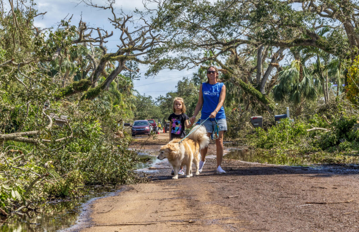 Olivia Chasse with her daughter Charlotte, walk their golden retriever Ben down Dahlia Lane in Vero Beach, Fla., on Saturday. Ben is a retired therapy dog, and the Chasses took him out walk to help cheer people up after tornadoes from Hurricane Milton damaged many Vero Beach homes earlier in the week.