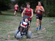 Camas High School&rsquo;s Ben Voogt pushes teammate Micah Snell in his wheelchair as they compete in a cross-country meet Oct.