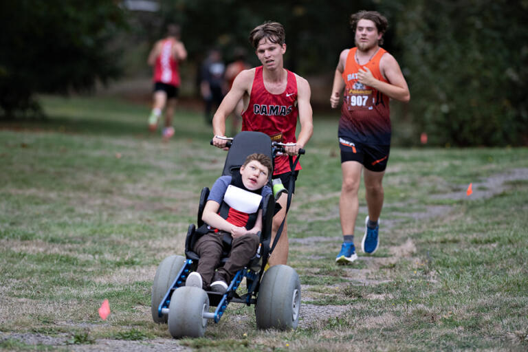 Camas High School’s Ben Voogt pushes teammate Micah Snell in his wheelchair as they compete in a cross-country meet Oct. 15 at UL Campus.