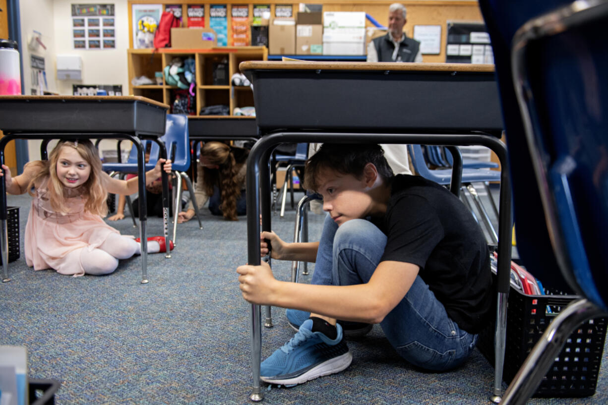 Maple Grove Primary School fourth-graders Mya Bagent, left, and Lincoln MacDonald, both 9, take shelter under their desks during an earthquake drill in Battle Ground on Thursday morning. The pair are among the students who took part in the Great ShakeOut Earthquake Drill, which took place at 10:17 a.m. statewide.