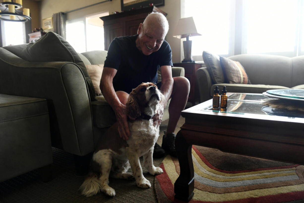 John Kofel pets his dog Kirby before giving Kirby his daily dosage of CBD and THC oils, which sit on the table next to him at right, at his home in Aurora, Colo. (Helen H.