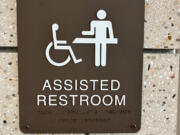 A sign outside a bathroom at a rest stop near Pacific Junction, Iowa, includes two icons: one of a person in a wheelchair and the other of a person preparing to use an adult-size changing table. Iowa is installing such changing tables at rest stops to better serve people with disabilities.