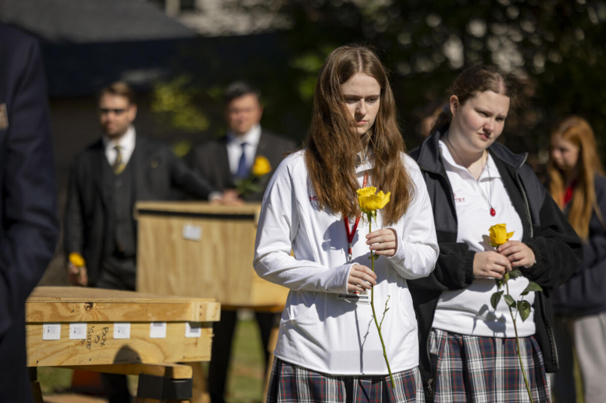 Participants hold yellow roses Oct. 16 alongside caskets during a committal service organized by Cook County officials and the Archdiocese of Chicago in which six unidentified people and 95 cremated indigent remains were buried at Mount Olivet Cemetery in Chicago.