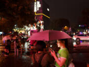 FILE - People look at their phones while waiting to cross an intersection in the rain at the Taikoo Li Sanlitun shopping center in Beijing, July, 30, 2024.