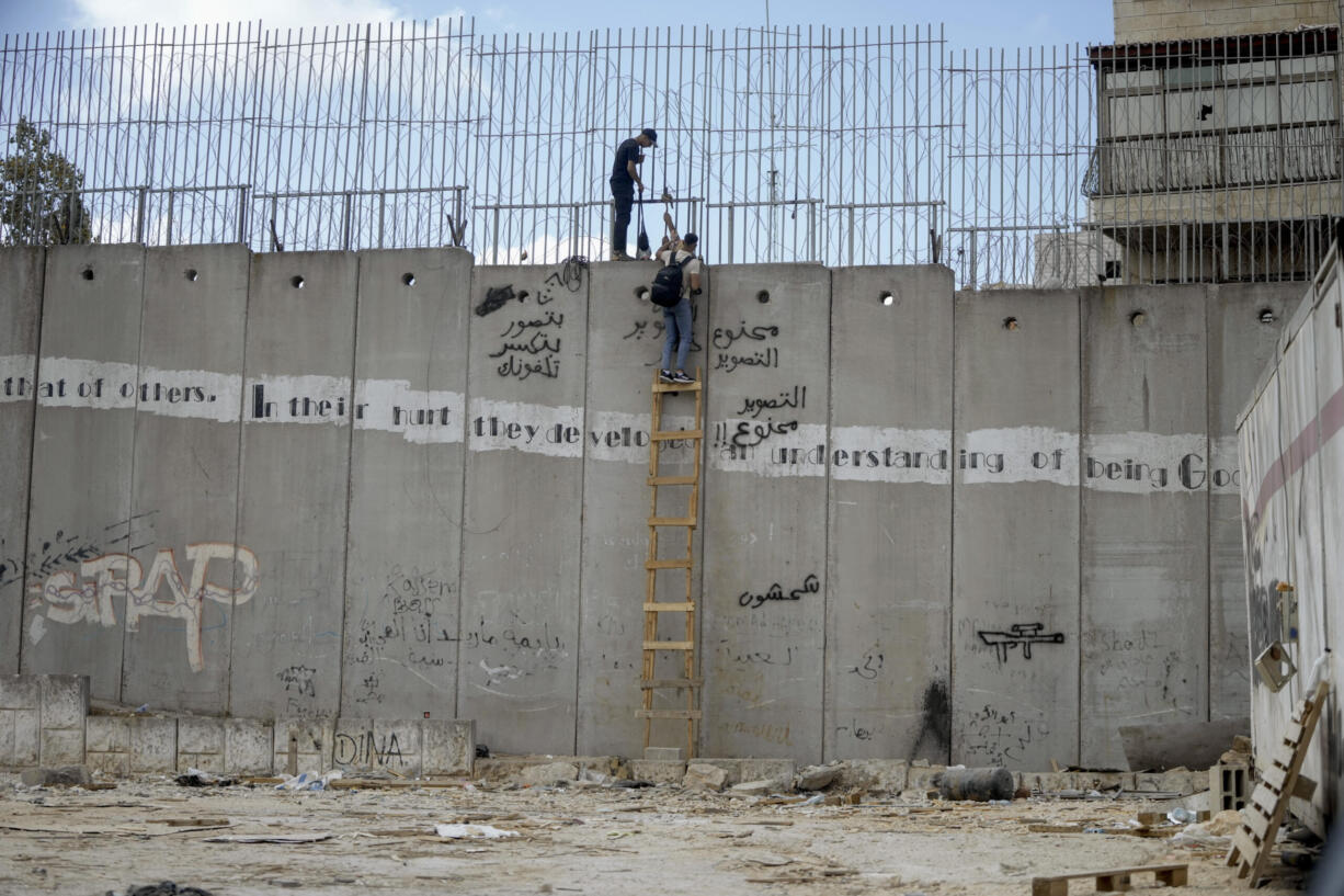 Palestinian men climb the separation wall at the town of al-Ram to illegally cross into Jerusalem, Sunday, Sept. 15, 2024.