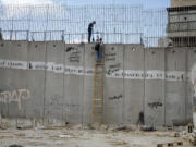 Palestinian men climb the separation wall at the town of al-Ram to illegally cross into Jerusalem, Sunday, Sept. 15, 2024.