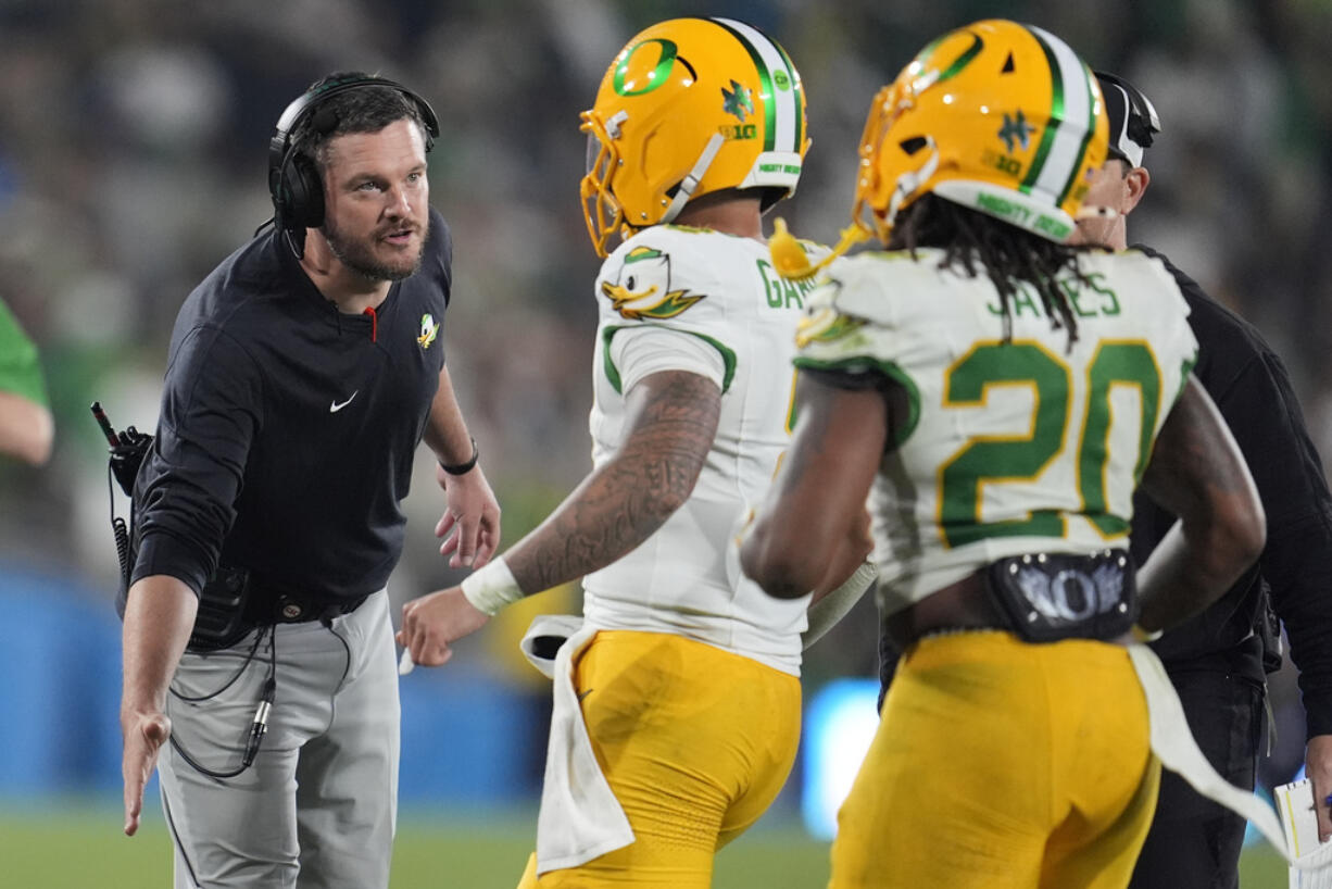 Oregon head coach Dan Lanning, left, shakes hands with quarterback Dillon Gabriel, center, after Gabriel threw a touchdown pass during the second half of an NCAA college football game against UCLA, Saturday, Sept. 28, 2024, in Pasadena, Calif.