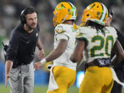 Oregon head coach Dan Lanning, left, shakes hands with quarterback Dillon Gabriel, center, after Gabriel threw a touchdown pass during the second half of an NCAA college football game against UCLA, Saturday, Sept. 28, 2024, in Pasadena, Calif.