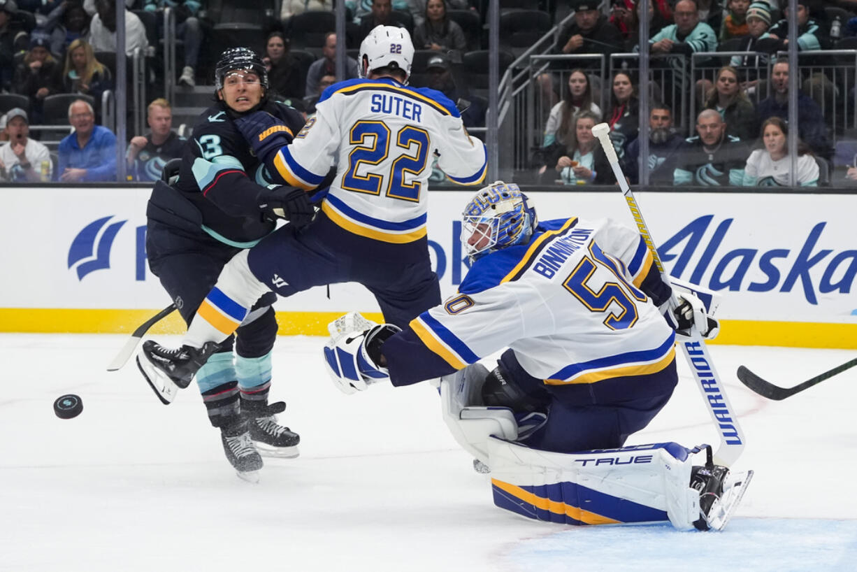 St. Louis Blues goaltender Jordan Binnington (50) looks on as the puck flies out of reach and defenseman Ryan Suter (22) and Seattle Kraken left wing Brandon Tanev, left, collide during the second period of an NHL hockey game Tuesday, Oct. 8, 2024, in Seattle.