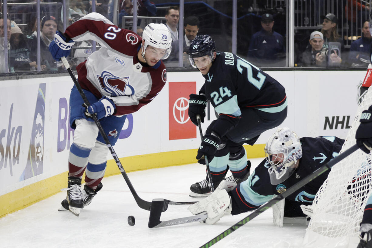 Seattle Kraken goaltender Philipp Grubauer, right, tries to push the puck away as defenseman Jamie Oleksiak (24) and Colorado Avalanche center Ross Colton (20) skate for it during the second period of an NHL hockey game, Tuesday, Oct. 22, 2024, in Seattle.