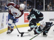 Seattle Kraken goaltender Philipp Grubauer, right, tries to push the puck away as defenseman Jamie Oleksiak (24) and Colorado Avalanche center Ross Colton (20) skate for it during the second period of an NHL hockey game, Tuesday, Oct. 22, 2024, in Seattle.