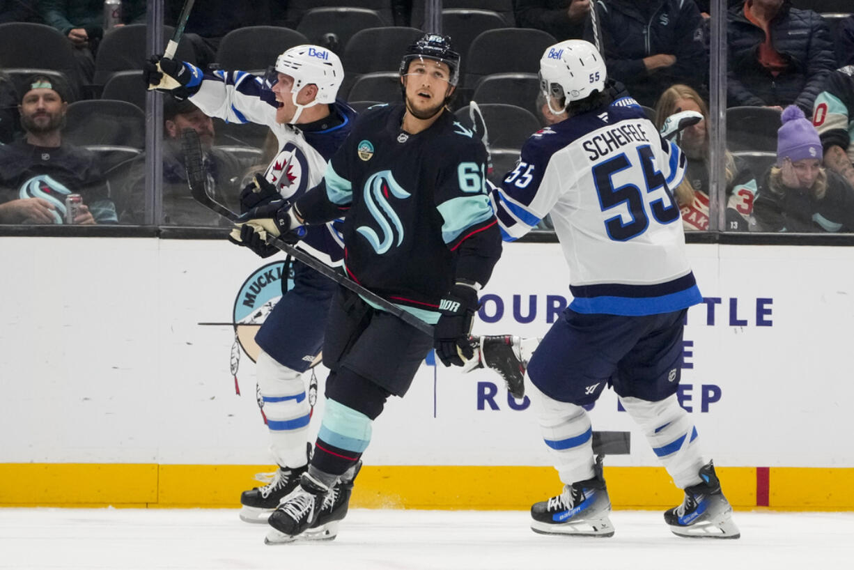 Winnipeg Jets left wing Nikolaj Ehlers, left, celebrates his game-winning goal with center Mark Scheifele (55) as Seattle Kraken defenseman Brandon Montour, center, looks away during overtime of an NHL hockey game Thursday, Oct. 24, 2024, in Seattle. The Jets won 4-3 in overtime.