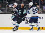 Winnipeg Jets left wing Nikolaj Ehlers, left, celebrates his game-winning goal with center Mark Scheifele (55) as Seattle Kraken defenseman Brandon Montour, center, looks away during overtime of an NHL hockey game Thursday, Oct. 24, 2024, in Seattle. The Jets won 4-3 in overtime.