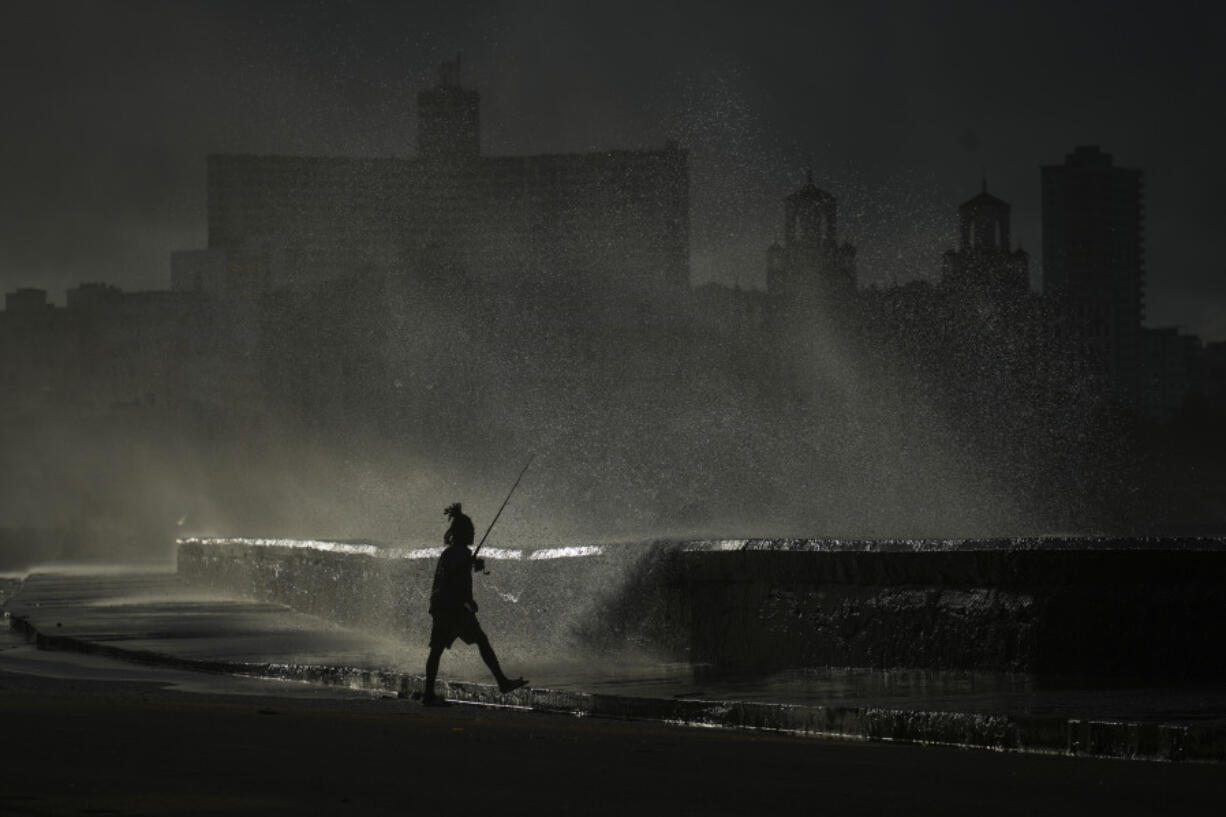 A person fishes along the boardwalk as waves crash during a power outage in Havana, Monday, Oct. 21, 2024.