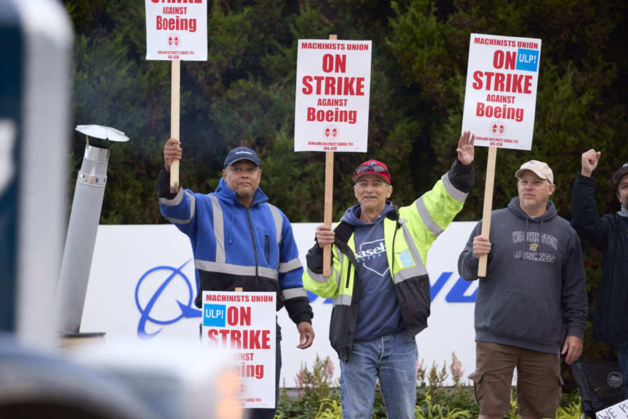 Boeing Machinists Union members Steven Wilson, left, Dave Hendrickson, center,, and Mark Erickson, right, wave to passing traffic while on the picket line at the Renton assembly plant, Friday, Sept. 13, 2024, in Renton, Wash.