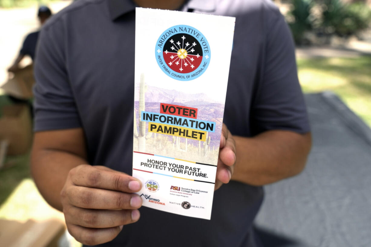 Alexander Castillo-Nunez, a civic engagement coordinator at the Inter Tribal Council of Arizona, Inc., shows a voter information pamphlet at an Arizona Native Vote booth during an Indigenous Peoples&rsquo; Day event, Monday, Oct. 14, 2024, in Phoenix. (AP Photo/Ross D.