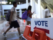 People walk past a Vote sign on the first day of early voting in the general election, Oct. 21, 2024, in Miami.