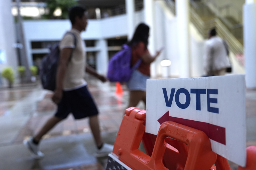 People walk past a Vote sign on the first day of early voting in the general election, Oct. 21, 2024, in Miami.