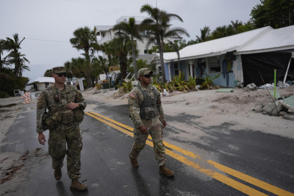 Members of the Florida Army National Guard walk past a home slated for demolition after being damaged in Hurricane Helene, as they check for any remaining residents, ahead of the arrival of Hurricane Milton, Tuesday, Oct. 8, 2024, on Anna Maria Island, Fla.