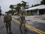 Members of the Florida Army National Guard walk past a home slated for demolition after being damaged in Hurricane Helene, as they check for any remaining residents, ahead of the arrival of Hurricane Milton, Tuesday, Oct. 8, 2024, on Anna Maria Island, Fla.