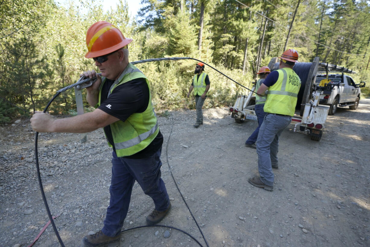 FILE - Carl Roath, left, a worker with the Mason County (Wash.) Public Utility District, pulls fiber optic cable on a project to install broadband internet service in the area surrounding Lake Christine near Belfair, Wash., on Aug. 4, 2021. (AP Photo/Ted S.