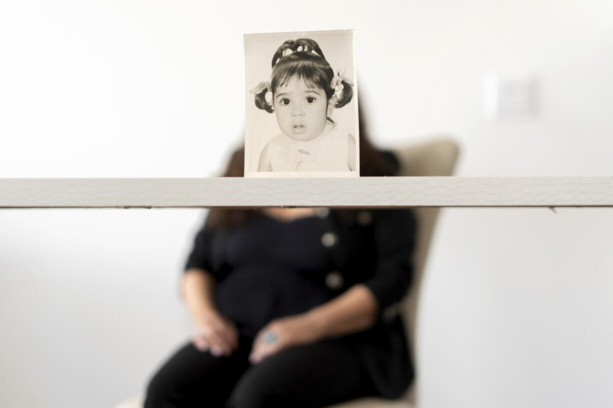 Buttons, who the Associated Press is referring to only by her childhood nickname because of her legal status, sits for a portrait behind her baby photo taken before she was adopted from Iran to a family in America, Monday, June 24, 2024, in Henderson, Nev. Buttons is one of thousands of children adopted from abroad by American parents, many of them military service members, who were left without citizenship by loopholes in American law that Congress has been aware of for decades, yet remains unwilling to fix.