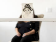 Buttons, who the Associated Press is referring to only by her childhood nickname because of her legal status, sits for a portrait behind her baby photo taken before she was adopted from Iran to a family in America, Monday, June 24, 2024, in Henderson, Nev. Buttons is one of thousands of children adopted from abroad by American parents, many of them military service members, who were left without citizenship by loopholes in American law that Congress has been aware of for decades, yet remains unwilling to fix.