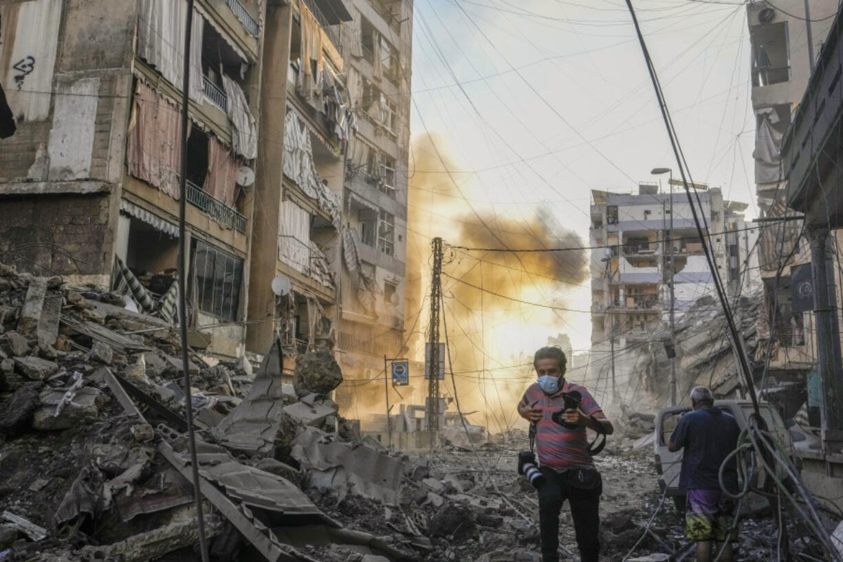 A photographer runs for cover as a smoke raises in the background following an Israeli airstrike in Dahiyeh, Beirut, Lebanon, Friday, Oct. 4, 2024.