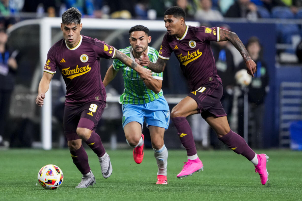 Portland Timbers forward Felipe Mora (9) pushes to the goal with forward Antony, right, after winning the ball from Seattle Sounders midfielder Cristian Roldan, center, after during the first half of an MLS soccer match Saturday, Oct. 19, 2024, in Seattle.