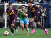 Portland Timbers forward Felipe Mora (9) pushes to the goal with forward Antony, right, after winning the ball from Seattle Sounders midfielder Cristian Roldan, center, after during the first half of an MLS soccer match Saturday, Oct. 19, 2024, in Seattle.