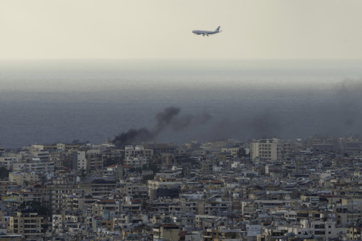 A Middle East Airlines airplane flies over Beirut as smoke rises from Israeli airstrikes in Dahiyeh, Beirut, Tuesday, Oct. 1, 2024.