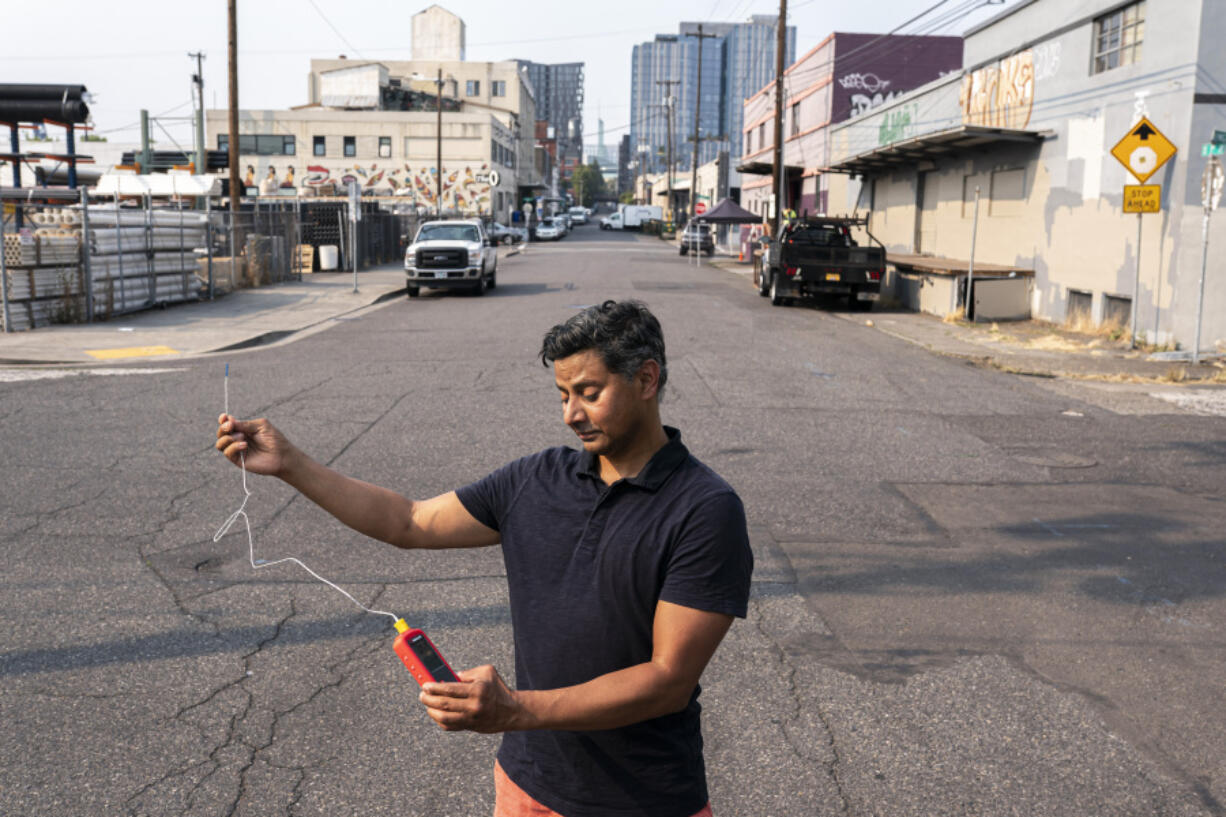 FILE - Vivek Shandas, a professor of climate adaptation at Portland State University, takes a temperature reading of almost 106 degrees in downtown Portland, Ore., Aug. 12, 2021.