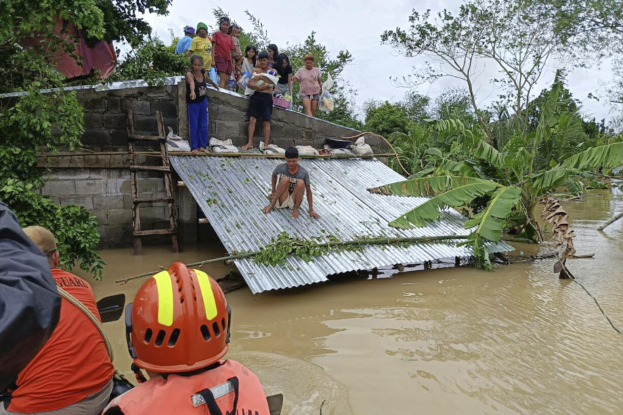 In this photo provided by the Philippine Coast Guard, residents staying on top of their roofs to avoid floods caused by Tropical Storm Trami, locally named Kristine, await to be rescued at Libon, Albay province, Philippines on Wednesday Oct. 23, 2024.