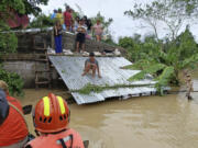 In this photo provided by the Philippine Coast Guard, residents staying on top of their roofs to avoid floods caused by Tropical Storm Trami, locally named Kristine, await to be rescued at Libon, Albay province, Philippines on Wednesday Oct. 23, 2024.