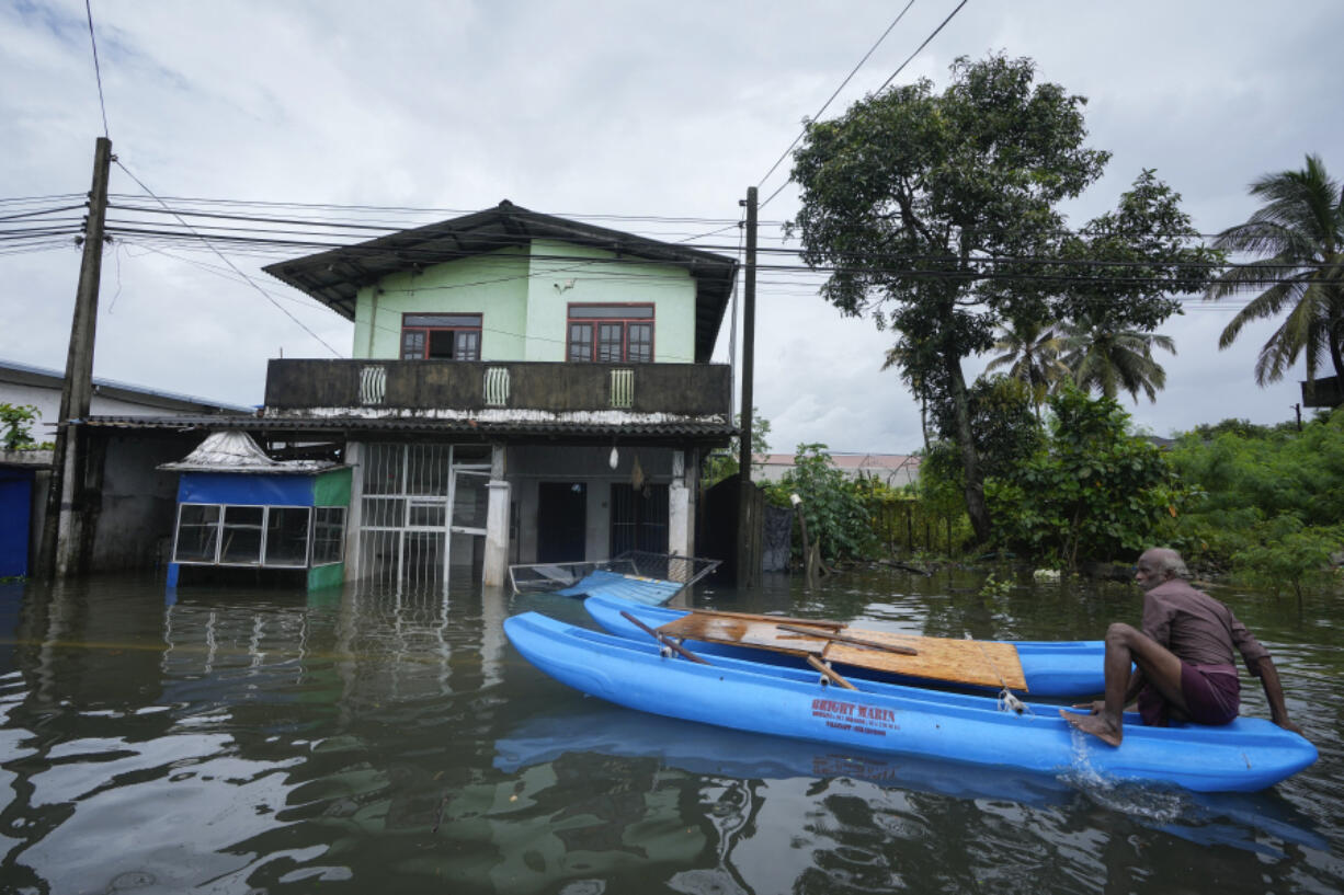 A man sits on a catamaran next to a damaged house in a flooded area in Colombo, Sri Lanka, Monday, Oct. 14, 2024.