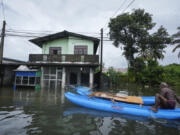 A man sits on a catamaran next to a damaged house in a flooded area in Colombo, Sri Lanka, Monday, Oct. 14, 2024.