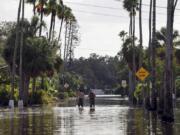 FILE - Men walk down a street flooded by Hurricane Helene in the Shore Acres neighborhood Sept. 27, 2024, in St. Petersburg, Fla.