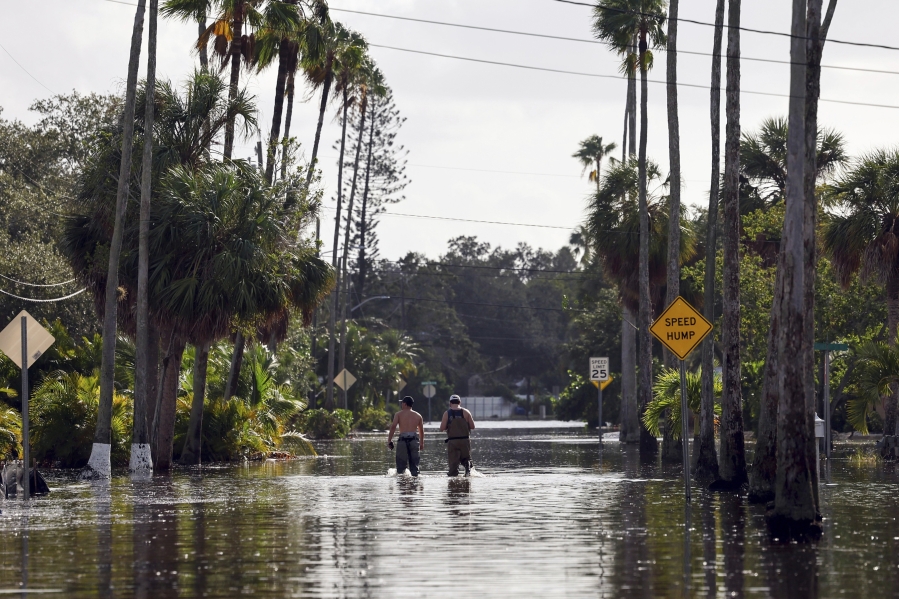 FILE - Men walk down a street flooded by Hurricane Helene in the Shore Acres neighborhood Sept. 27, 2024, in St. Petersburg, Fla.