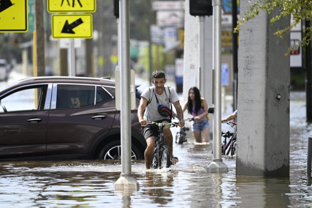 FILE - Mica Martell, left, and his niece and nephews ride bicycles through a flooded neighborhood, Sept. 27, 2024, in Crystal River, Fla. (AP Photo/Phelan M.