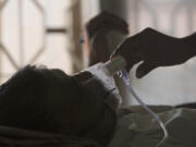 FILE - A relative adjusts the oxygen mask of a tuberculosis patient at a TB hospital on World Tuberculosis Day in Hyderabad, India, March 24, 2018.