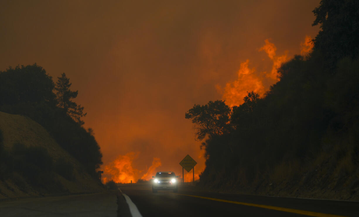 FIRE - The Line Fire jumps highway 330 as a motorist speeds past Saturday, Sept. 7, 2024, near Running Springs, Calif.