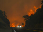 FIRE - The Line Fire jumps highway 330 as a motorist speeds past Saturday, Sept. 7, 2024, near Running Springs, Calif.