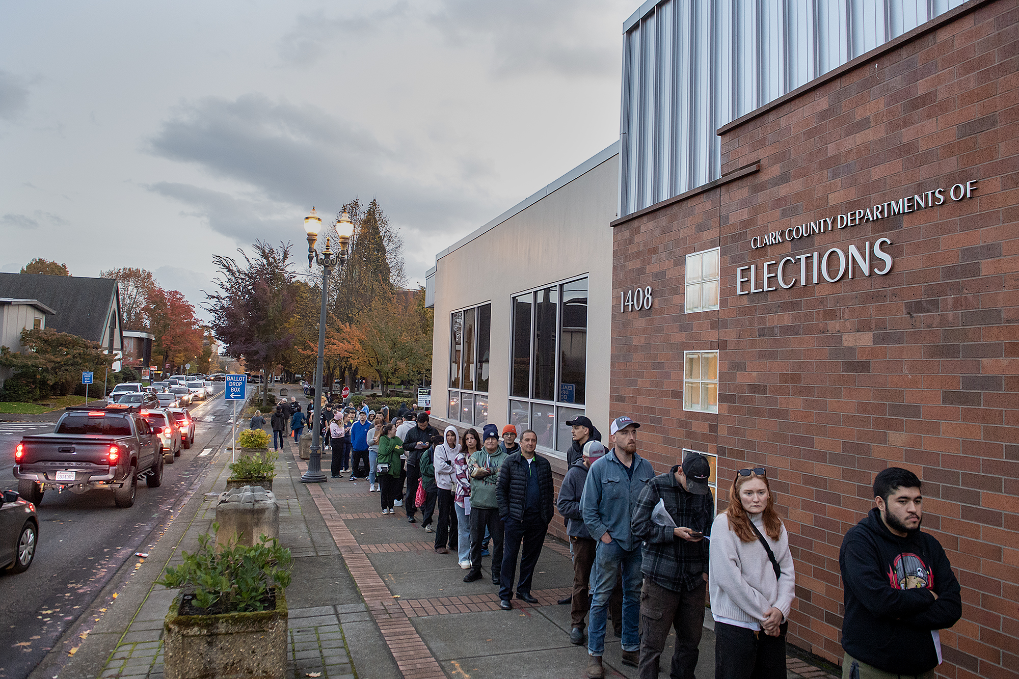 Motorists wait to drop off their ballots, left, as people stand in line to register to vote at the elections office in downtown Vancouver on Monday evening, Nov. 4, 2024.