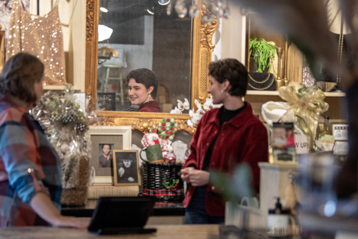 Sales associate Olivia Ovall, in red, is reflected in a mirror as she checks out some of the items for sale as Not Too Shabby in Vancouver gears up for the holidays. Clark County retailers hired about 450 people between October and December last year, according to data from the Washington Employment Security Department.