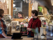 Sales associate Olivia Ovall, in red, is reflected in a mirror as she checks out some of the items for sale as Not Too Shabby in Vancouver gears up for the holidays. Clark County retailers hired about 450 people between October and December last year, according to data from the Washington Employment Security Department.