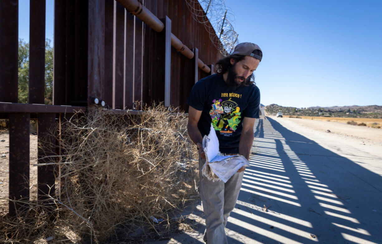 Pete Cerep, 37, looks at documents he found at the U.S.-Mexico border wall as a Border Patrol vehicle drives nearby on Tuesday in Jacumba Hot Springs. Cerep has lived in the area just under two years and said he didn&rsquo;t know the area was used by migrants to enter into the United States until moving there.