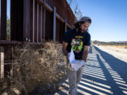 Pete Cerep, 37, looks at documents he found at the U.S.-Mexico border wall as a Border Patrol vehicle drives nearby on Tuesday in Jacumba Hot Springs. Cerep has lived in the area just under two years and said he didn&rsquo;t know the area was used by migrants to enter into the United States until moving there.