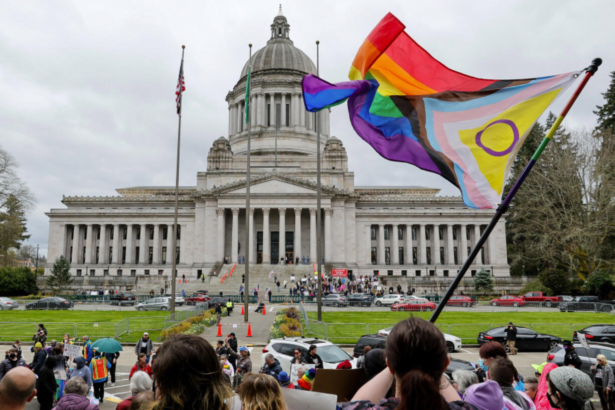 A supporter of trans rights waves a flag in front of the Temple of Justice as an opposing rally for opponents of legislation to exempt youth shelters from contacting parents of kids seeking gender-affirming health care gathers on the steps of the Capitol Building on April 21, 2023, in Olympia, Washington.